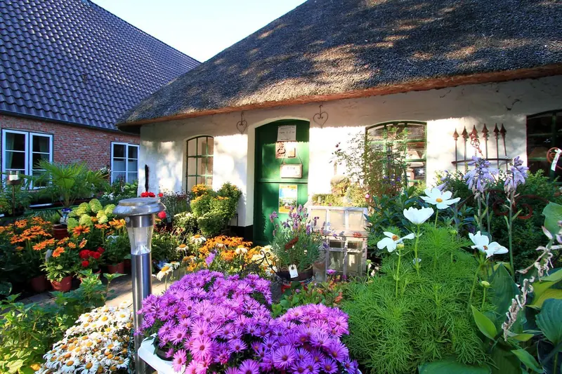 Der Landladen Kühl von außen, umgeben von blühenden Beeten vor dem reetgedeckten Haubarg